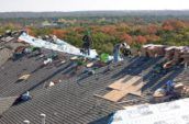 team of roofers working across large roof with tree covered scenery in the background