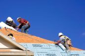 four roofers working on top of house with clear blue sky in the background
